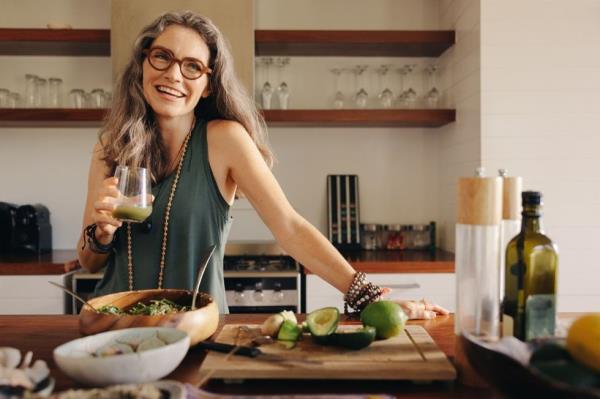 Healthy senior woman smiling while holding some green juice in her kitchen